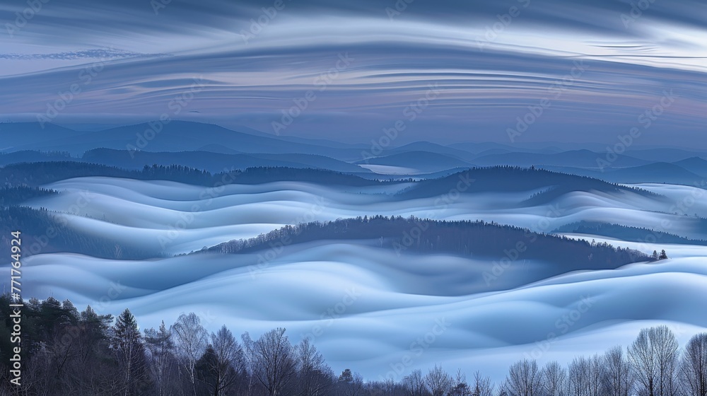 Obraz premium A foggy mountain range with trees in the foreground and a cloudy sky