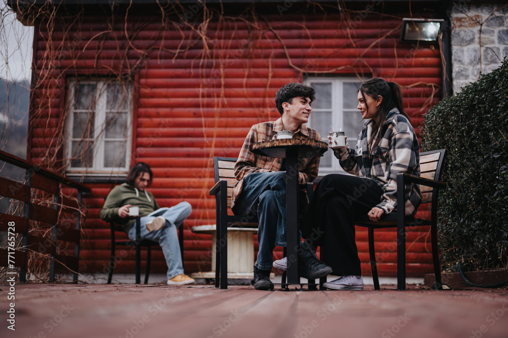 Young couple sharing a moment with hot beverages on a rustic cabin's front porch, exuding warmth and happiness. Young couple sharing a moment with hot beverages on a rustic cabin's front porch, exuding warmth and happiness.