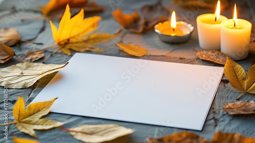 A cozy autumn-themed setting with candles and fallen leaves surrounding a blank piece of paper photo