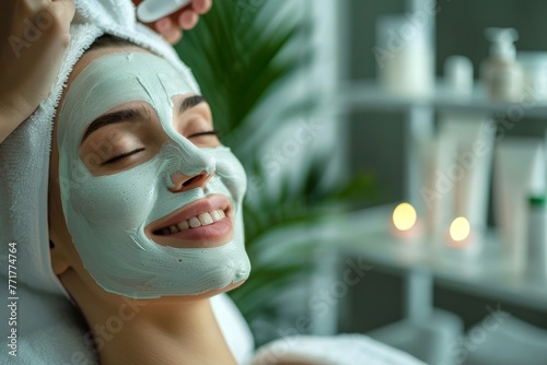 Beautiful young woman's face with facial mask and towel on the head. Woman gets facial care by beautician at spa salon. Face peeling mask, spa beauty treatment, skincare. Close-up, side view.