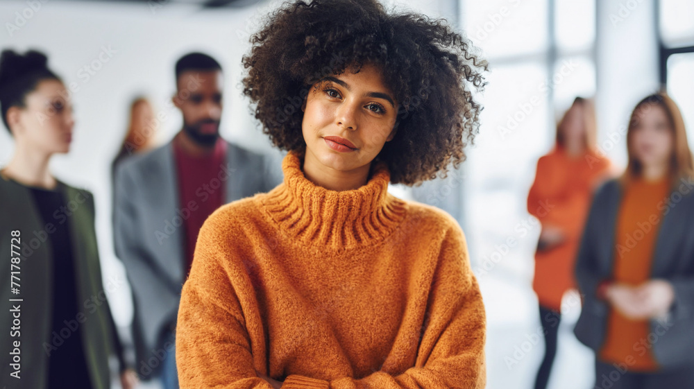 Fototapeta premium A young adult multi-ethnic woman wearing an orange turtleneck sweater, standing in the middle of the office surrounded and stared at by work colleagues, deep in thought and daydreaming