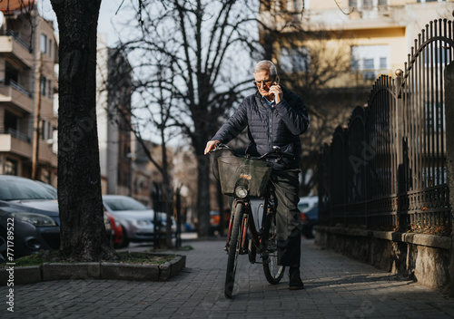 Senior man on phone while walking with bicycle on urban street.
