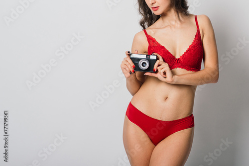 Beautiful female with pretty smile in red lingerie holding photo camera, isolated on white