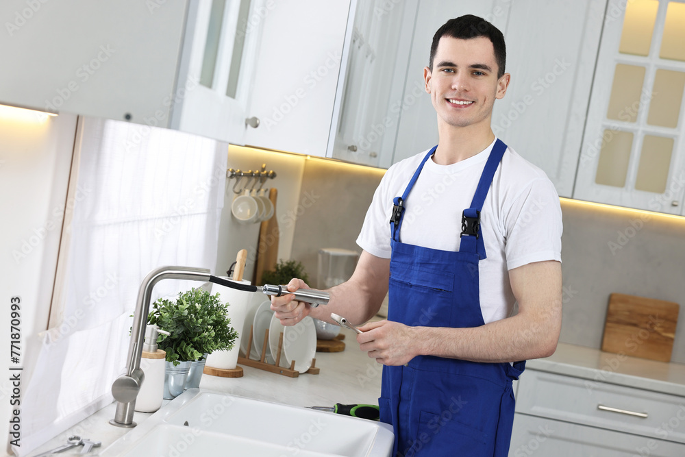 Smiling plumber repairing faucet with spanner in kitchen - obrazy, fototapety, plakaty 