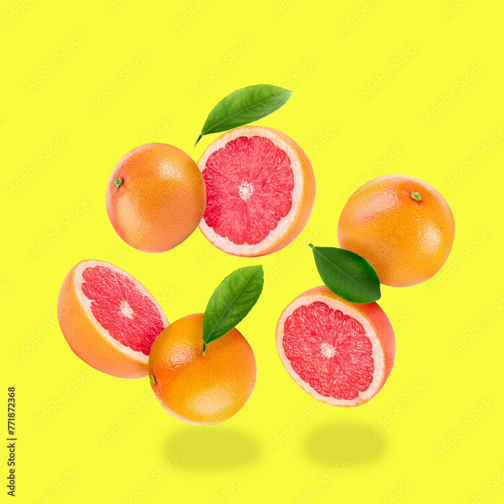 Fresh ripe grapefruits and green leaves falling on yellow background - obrazy, fototapety, plakaty 