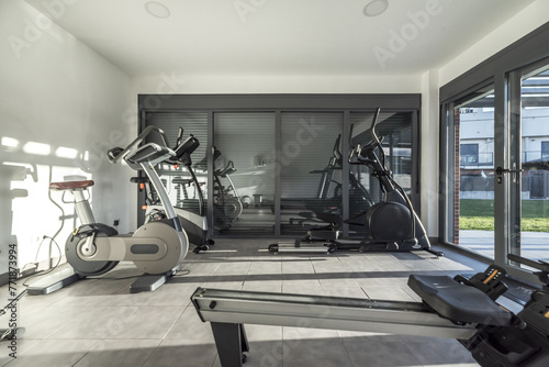 Small gym with several exercise machines in a building with large windows with blinds