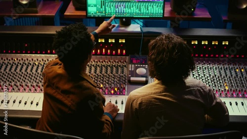 Team of sound engineers working on recording and editing tracks in professional studio control room, collaborating on mix and master audio files. Musician and technician pressing sliders. Camera B. photo