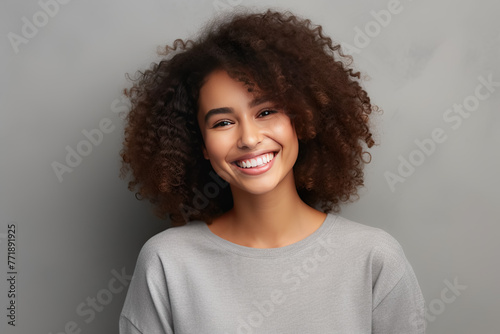  Radiant Young Woman with Curly Hair Smiling Cheerfully Against a Grey Background