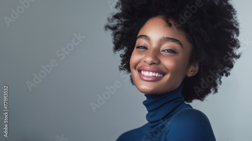 A beautiful African American female model with a broad smile and wearing a blue turtleneck shirt. She has a flawless complexion. Perfect teeth suggesting dental care. Copy space.. © Daniel L