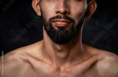 Close-up of a young man, bare-chested and shirtless, with a beard isolated on black background