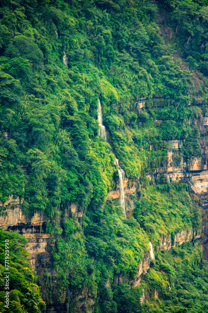 Lush greenery covers a steep cliff with cascading waterfalls in Barichara, Santander, Colombia
