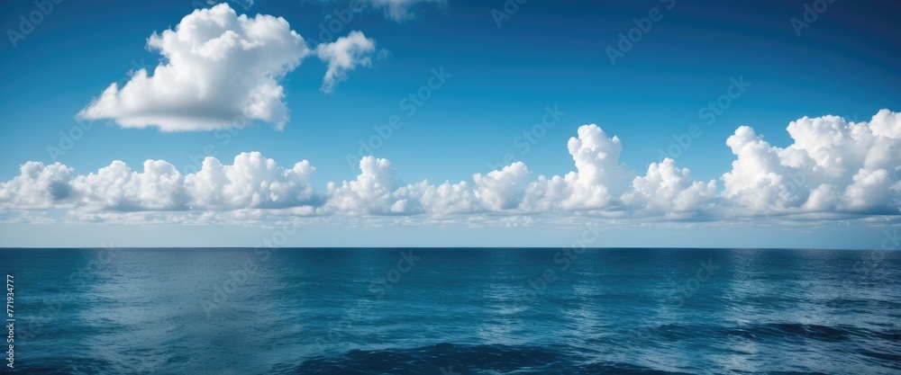 Obraz premium Capture the serene expanse of a blue sky with fluffy clouds drifting over the ocean