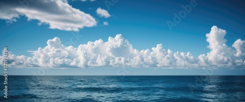 Capture the serene expanse of a blue sky with fluffy clouds drifting over the ocean