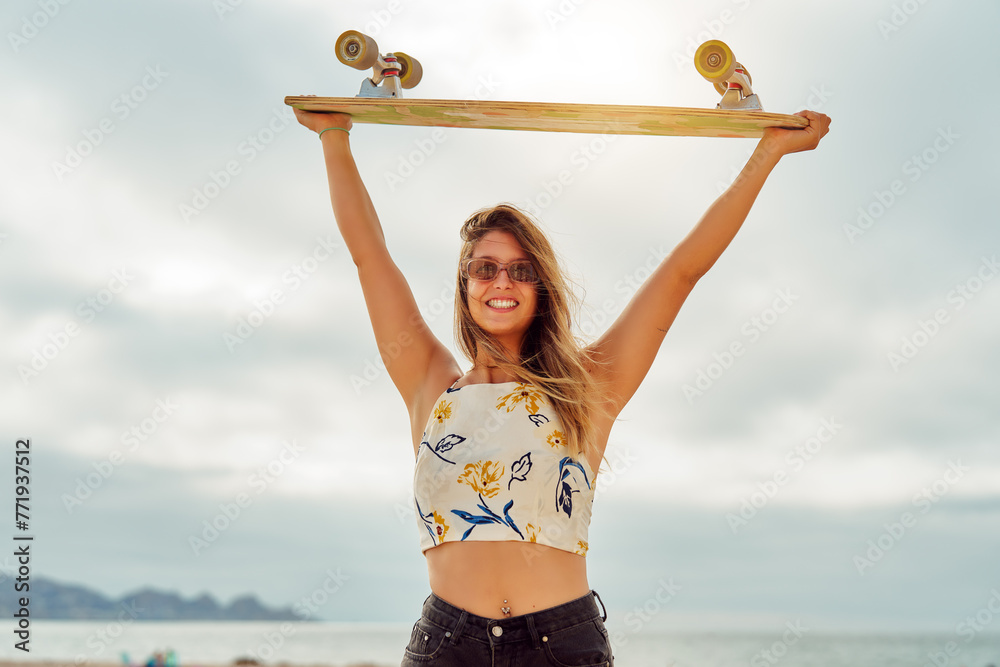portrait beautiful young woman holding surf skate board with hands above her head happy - obrazy, fototapety, plakaty 