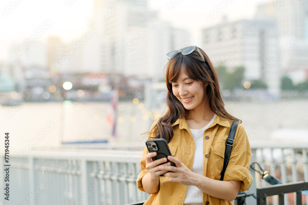 Fototapeta premium young Asian woman in 30s on a solo adventure. Technology in hand, she captures the essence of cultural exploration and joyful discovery.