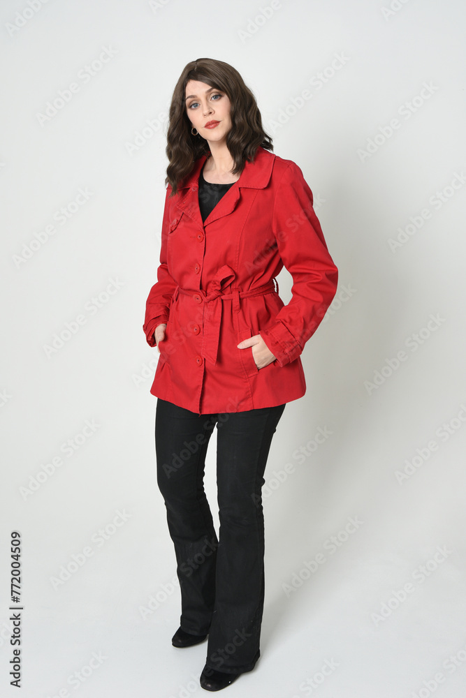 full length portrait of beautiful brunette woman model, wearing red trench coat jacket leather pants. standing pose, walking towards the camera. isolated on white studio background.