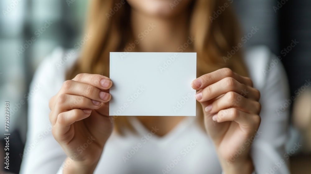 Mockup with beautiful manicured hands holding a 5 inches wide by 7 inches length, blank invitation card vertically, light background. - obrazy, fototapety, plakaty 