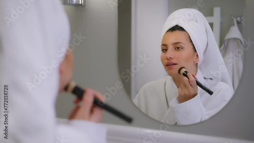 A young girl is getting her makeup done. A girl puts a blush on her face. The girl applies makeup with a brush. A woman is going to work. Morning makeup. Young beautiful girl makeup in front of the