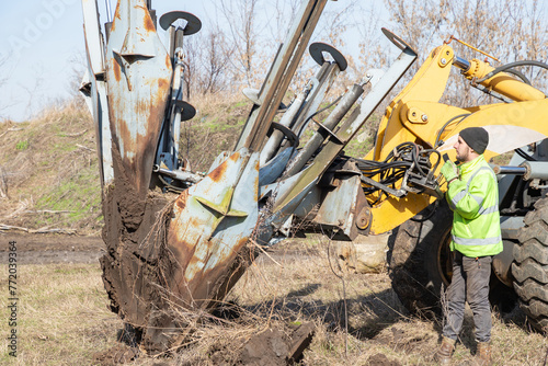 Male worker operates tree transplanter heavy machine. Landscaping, seasonal agricultural engineering, large trees landing machines. photo