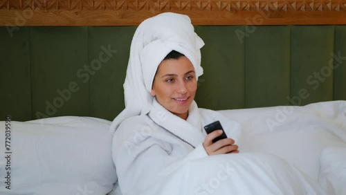 The girl is watching TV. A young girl dances to the music. A girl lying in bed and watching a movie. bed with a white bed. Vacation in a hotel room. Girl switches TV with remote control. High quality