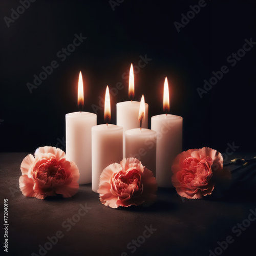Burning candles with carnation flowers on dark background. Mourning concept