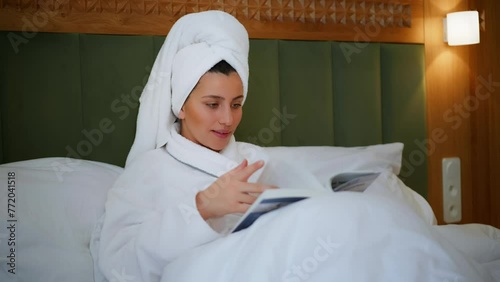 Young girl resting in bed. A girl reading a book. Vacation. Hotel room. Morning reading. A girl resting in the room and reading a book. A brunette girl is preparing for an exam. White bed. Cozy room