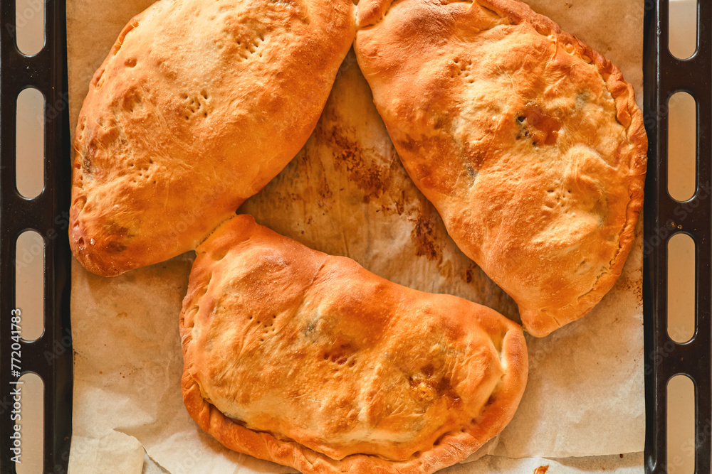 Homemade calzones cooling on a baking sheet, a delicious traditional Italian dessert and a gastronomic journey to Italy. Homemade calzones cooling on a baking sheet, a delicious traditional Italian dessert and a gastronomic journey to Italy.