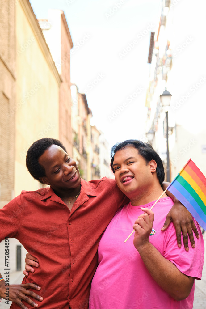 Happy gay couple are holding a rainbow flag and smiling during Pride Parade.