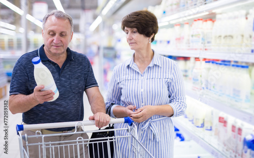 Mature family of retirees considering bottle of milk in dairy section of supermarket photo