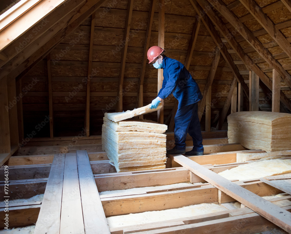 Roof insulation. A worker puts glass wool insulation in the attic. Roof insulation. A worker puts glass wool insulation in the attic.