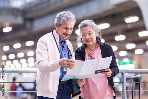Asian active senior retirement couple is looking at the map for direction inside airport terminal for second honeymoon pensioner travel and urban metro train transportation concept photo