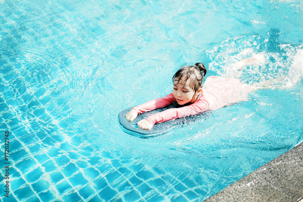 A little asian girl in swimming in the pool. Cute girl playing in outdoor swimming pool on a hot summer day. Kids learn to swim.