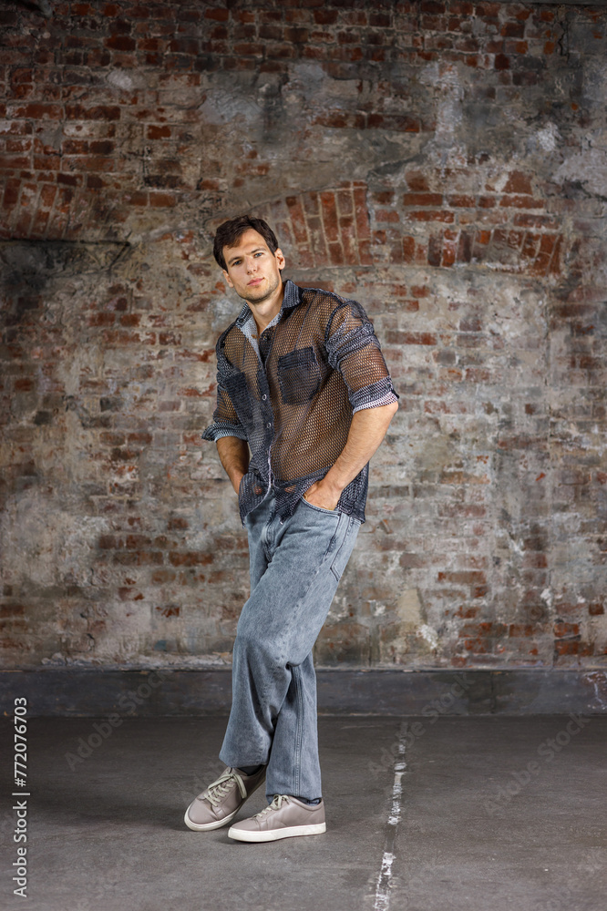 A modern young man with a stylish hairstyle stands near a wall on a dark background