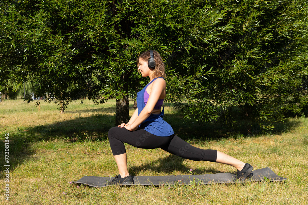 Female fitness instructor does, shows exercises in a green park. Sport concept.