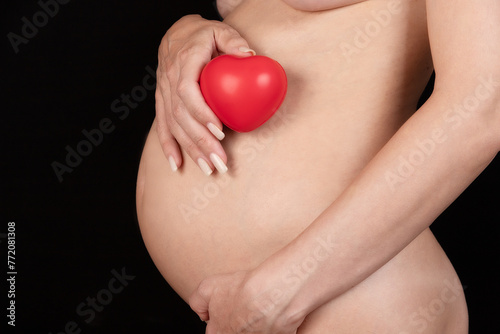 Naked pregnant woman holding a red heart in her hands. IVF, medicine and health concept.