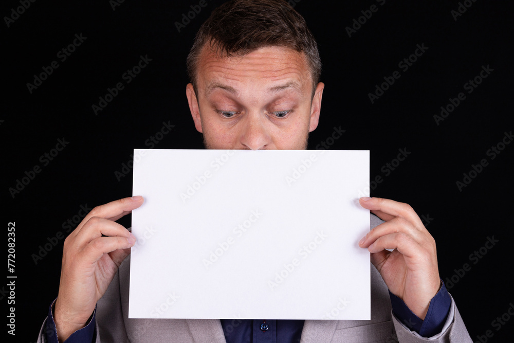 A man in a gray suit holds a blank sheet of paper with place for text in his hands on a black background. Business idea, concept. A man in a gray suit holds a blank sheet of paper with place for text in his hands on a black background. Business idea, concept.