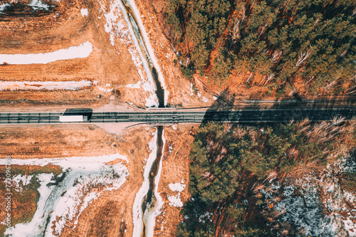 Aerial View Of Highway Road Through Spring Forest Landscape. Top View Of White Truck Tractor Unit Prime Mover Traction Unit In Motion On Freeway. Business Transportation, Trucking Industry. Flat View.