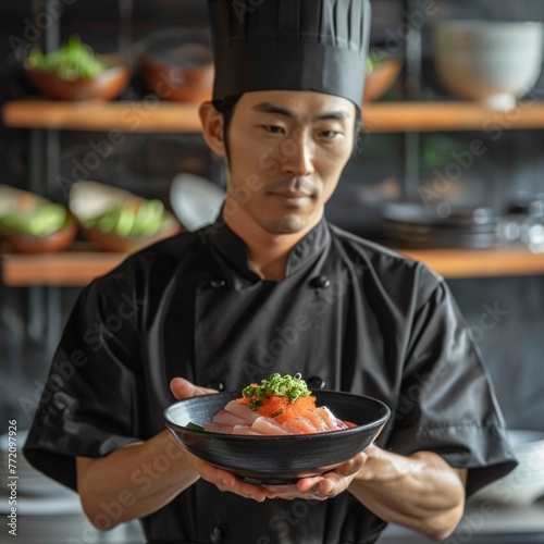 A Japanese food chef wears a black chef's uniform and holds a bowl of Japanese food in his hand.