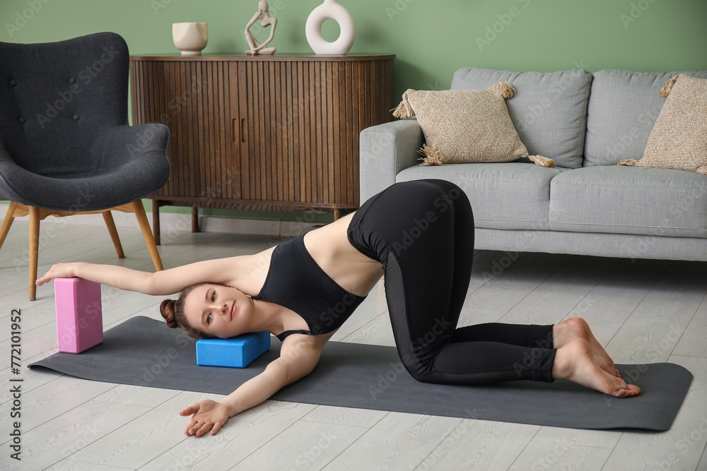 Fototapeta premium Sporty young woman practicing yoga with blocks at home