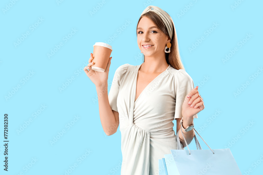 Beautiful stylish young woman with shopping bags and cup of coffee on blue background Beautiful stylish young woman with shopping bags and cup of coffee on blue background