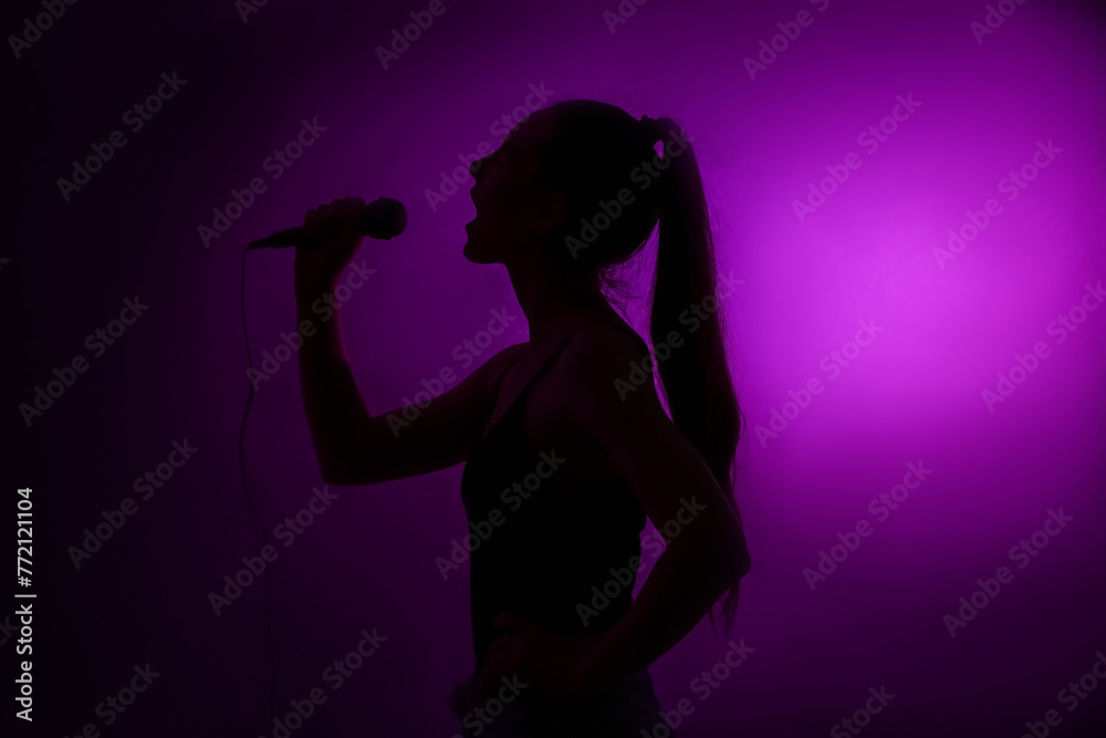 Silhouette of woman with modern microphone singing on dark background