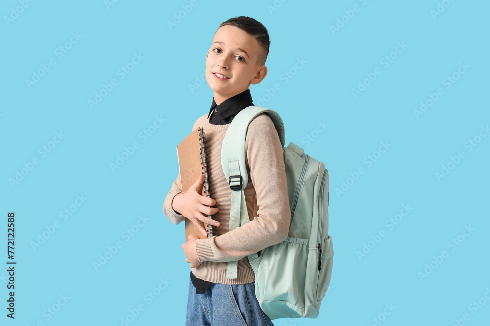 Cute schoolboy with backpack and notebook on blue background Cute schoolboy with backpack and notebook on blue background