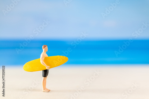 Miniature people man in a swimsuit, and holding a yellow surfboard on the beach