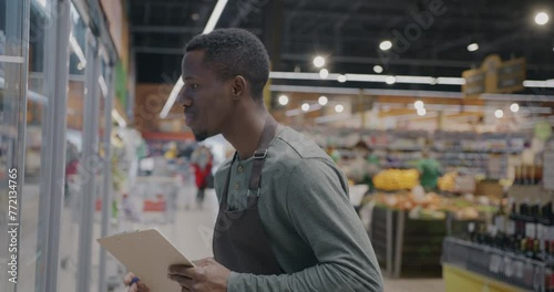 African American guy supermarket worker doing inventory writing information checking food. Retail business and consumption concept. photo