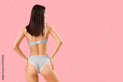 Slim young woman in grey cotton underwear on pink background, back view