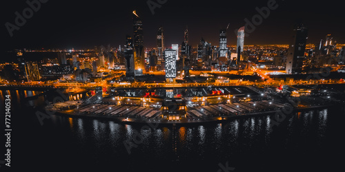 A colorful orange light aerial view of the Kuwait City skyline at night with a drone.