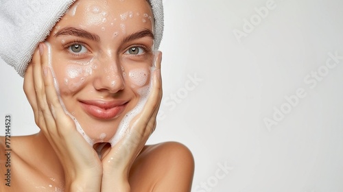 A white girl with a white towel wrapped on her head with soap suds on her face on a light background