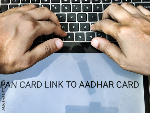 Picture of a person working on laptop. Placard with PAN CARD LINK TO AADHAR CARD written on it. photo