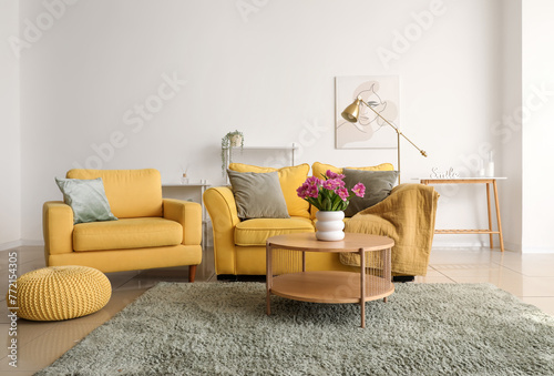 Interior of light living room with sofa, armchair and tulips on table © Pixel-Shot