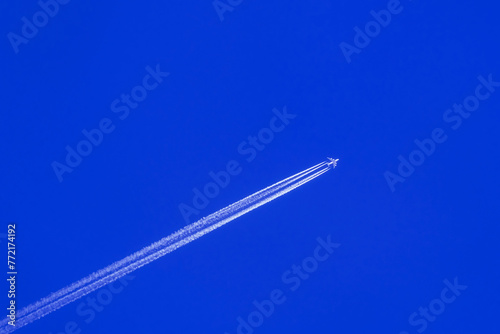 Airplane flying on deep cloudy blue sky with chemical direction trails, view from a distance